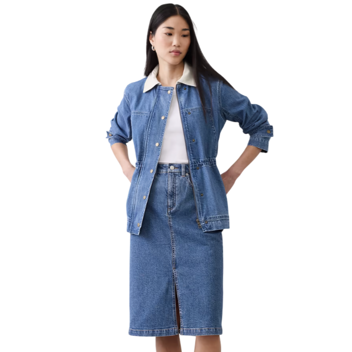A woman models a denim skirt and jacket set, featuring silver buttons and a white inner collar, paired with a white top.