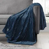 A plush, ribbed dark blue electric blanket drapes over a gray couch, featuring a power control symbol on its edge.