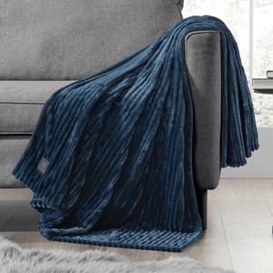 A plush, ribbed dark blue electric blanket drapes over a gray couch, featuring a power control symbol on its edge.