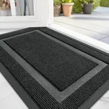 Black textured doormat placed at a doorway with visible outdoor pots and plants.