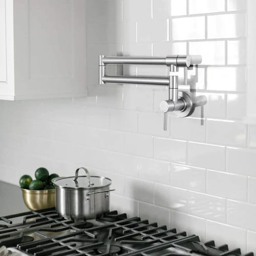 A wall-mounted pot filler faucet above a stove with a stainless steel pot on the burner.