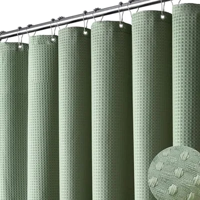 A green shower curtain with a textured, waffle-weave design, hanging on a metal rod using hooks. A close-up inset highlights the fabric pattern.