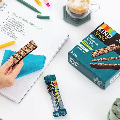 KIND Thins Bars, Dark Chocolate Nuts & Sea Salt flavor, are displayed beside a back-to-school shopping list, a coffee, and stationery items.