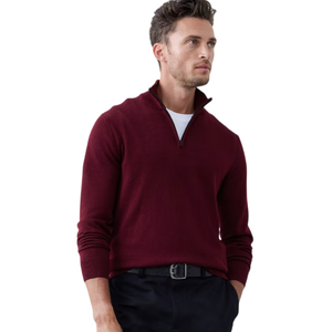 A person is wearing a burgundy quarter-zip sweater, a white undershirt, and black trousers with a belt. The outfit is simple and stylish against a plain background.