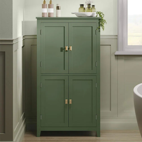 A green wooden floor storage cabinet with four doors and gold handles, topped with decorative items. It's positioned against wainscoting in a bathroom setting.