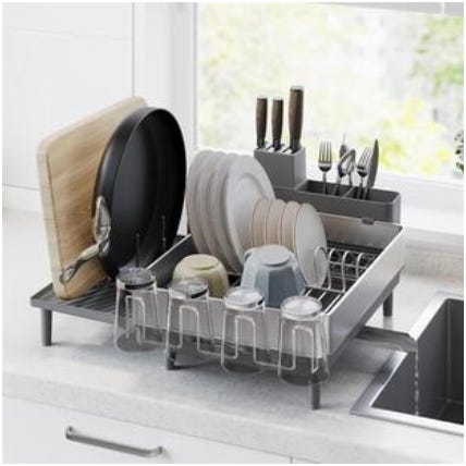 A countertop dish rack holds various kitchen items, including plates, bowls, cups, knives, forks, and a cutting board.