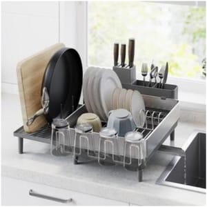 A countertop dish rack holds various kitchen items, including plates, bowls, cups, knives, forks, and a cutting board.