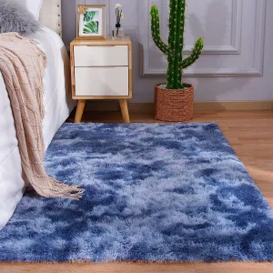 A blue and white fluffy rug is placed on a wooden floor next to a bed with a beige blanket. A small wooden nightstand with drawers holds decor items, next to a cactus in a woven basket.