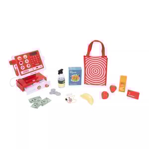 Toy cash register set with accessories including play money, coins, a scanner, a shopping bag with a bullseye design, faux cereal, fruit, a spray bottle, and an orange juice container.