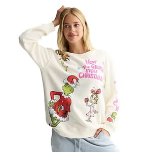 A woman wears a white sweatshirt featuring \“How The Grinch Stole Christmas!\“ graphics, including the Grinch in a Santa outfit and Cindy Lou Who, with cartoonish text.