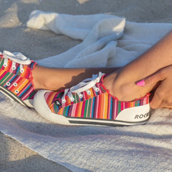 A person is wearing colorful striped sneakers on a sandy background.