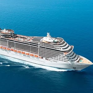 Cruise ship sailing on open blue water, featuring multiple decks and lifeboats along the sides.