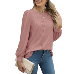 A woman wears a pink eyelet blouse with long sleeves and a round neckline, paired with blue jeans. She holds a beige clutch and wears a necklace and hoop earrings.