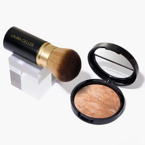 A bronzer compact with a mirror and a makeup brush labeled \“Laura Geller\“ with a gold accent handle are displayed on a white surface.