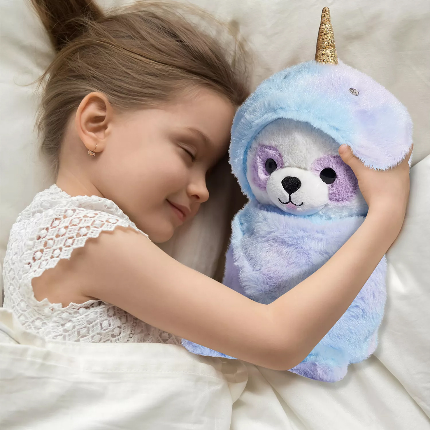 A child is cuddling a plush toy with a glittery unicorn horn and blue-purple fur, lying on a bed.