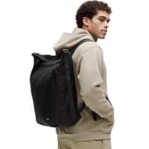 A man wearing a beige hoodie carries a black lululemon Convertible Backpack Tote, featuring a sleek and minimalist design. The tote can be worn as a backpack, providing versatility and ample storage with adjustable straps.