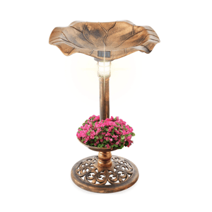 A bronze-colored birdbath with a solar light on top, featuring a design resembling a leaf. It includes a lower section filled with pink flowers and a decorative base.
