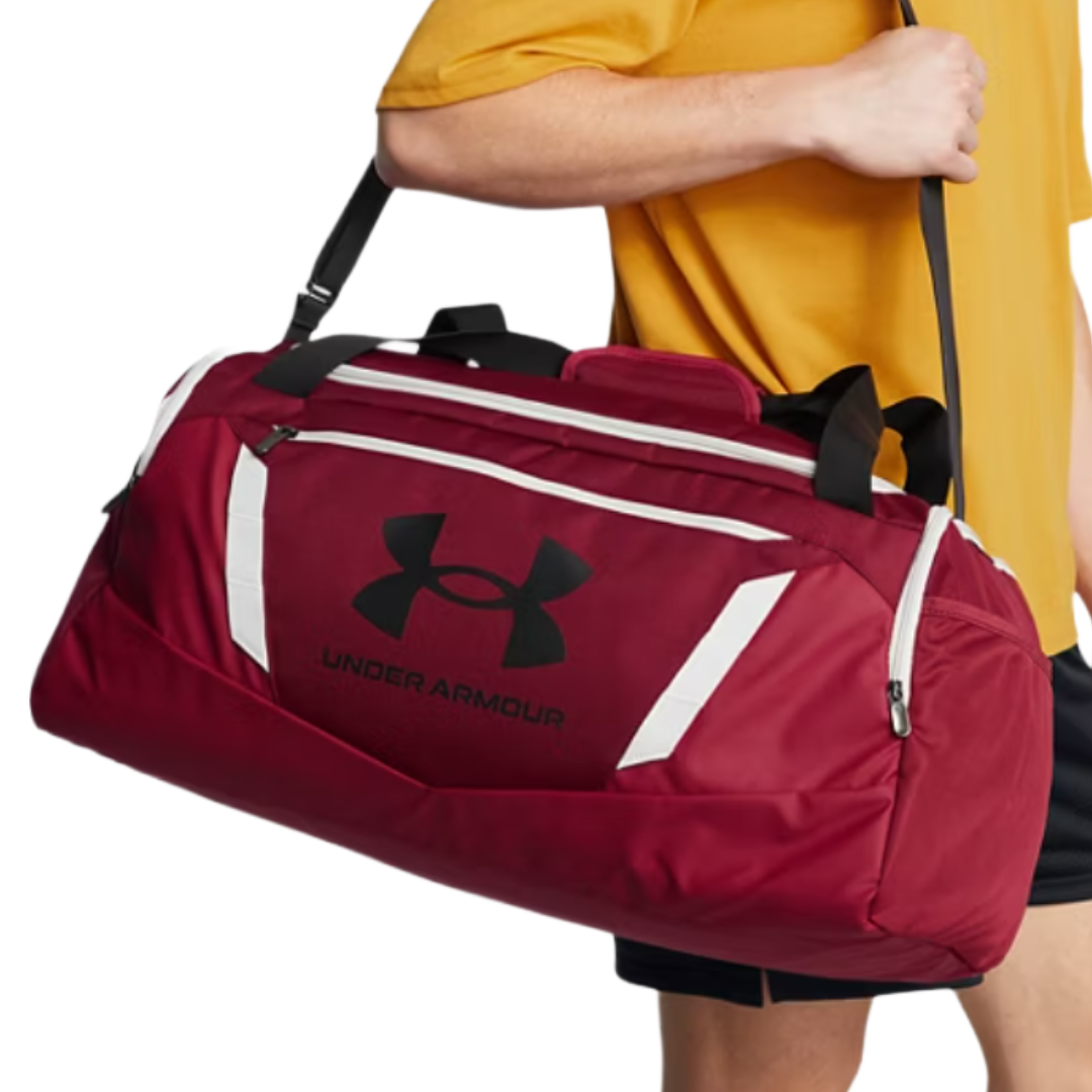 A red Under Armour duffel bag with black logo details, featuring white accent stripes and zippered pockets, carried by a person in a yellow shirt.