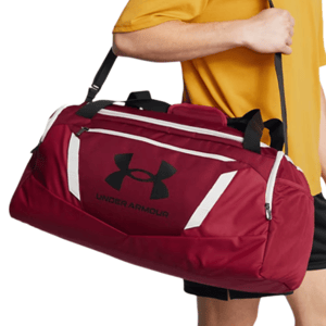 A red Under Armour duffel bag with black logo details, featuring white accent stripes and zippered pockets, carried by a person in a yellow shirt.