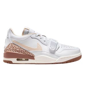 The Air Jordan Legacy 312 Low features a white upper with beige accents, a prominent Swoosh, and a brown outsole. The heel includes a patterned design with an air unit, offering a blend of classic and contemporary Jordan elements.