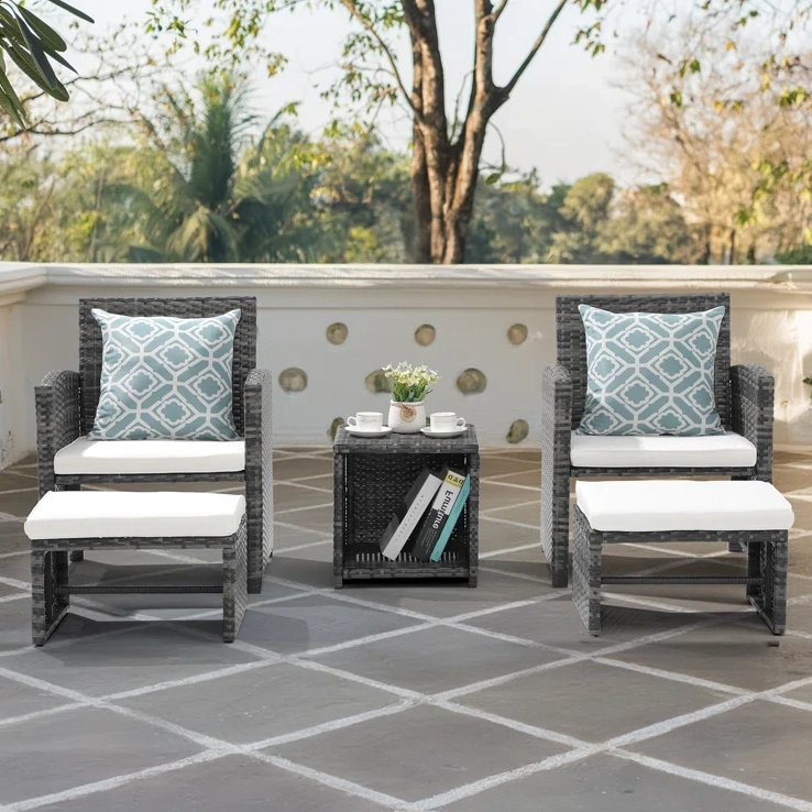 Outdoor furniture set with two wicker chairs, white cushions, patterned accent pillows, and a matching side table with decorative items.