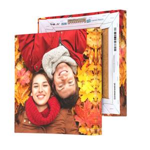 An 8\“ x 8\“ custom canvas print featuring a smiling couple lying on autumn leaves, showcasing a wooden frame with a wall-mounting hook on the back.