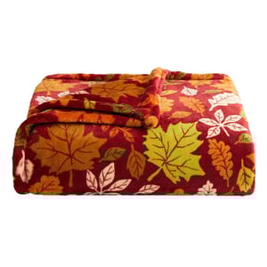 A folded fleece blanket featuring a pattern of autumn leaves in red, orange, green, and white on a maroon background.
