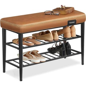 A brown cushioned bench with the brand name \“VASAGLE\“ features two metal racks for shoe storage, holding various pairs of shoes. On top, there are eyeglasses and a book.