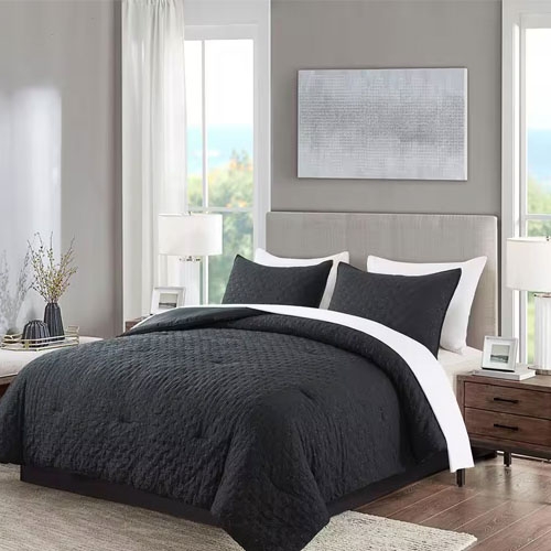 A bedroom with a gray upholstered headboard, framed artwork, and a dark comforter set with white accents.