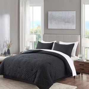A bedroom with a gray upholstered headboard, framed artwork, and a dark comforter set with white accents.