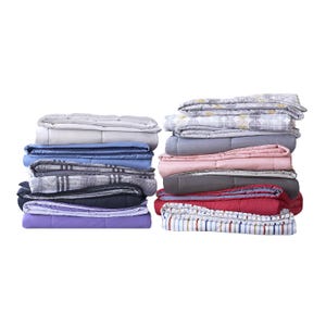 A variety of folded comforters in different colors and patterns are stacked neatly in two piles.