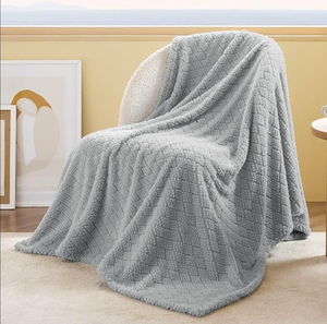 A soft, light gray throw blanket with a textured, diamond-patterned design is draped over a chair. The setting includes a bright, neutral-toned room with framed artwork nearby.