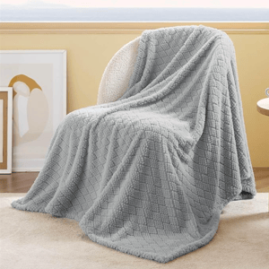 A soft, light gray throw blanket with a textured, diamond-patterned design is draped over a chair. The setting includes a bright, neutral-toned room with framed artwork nearby.