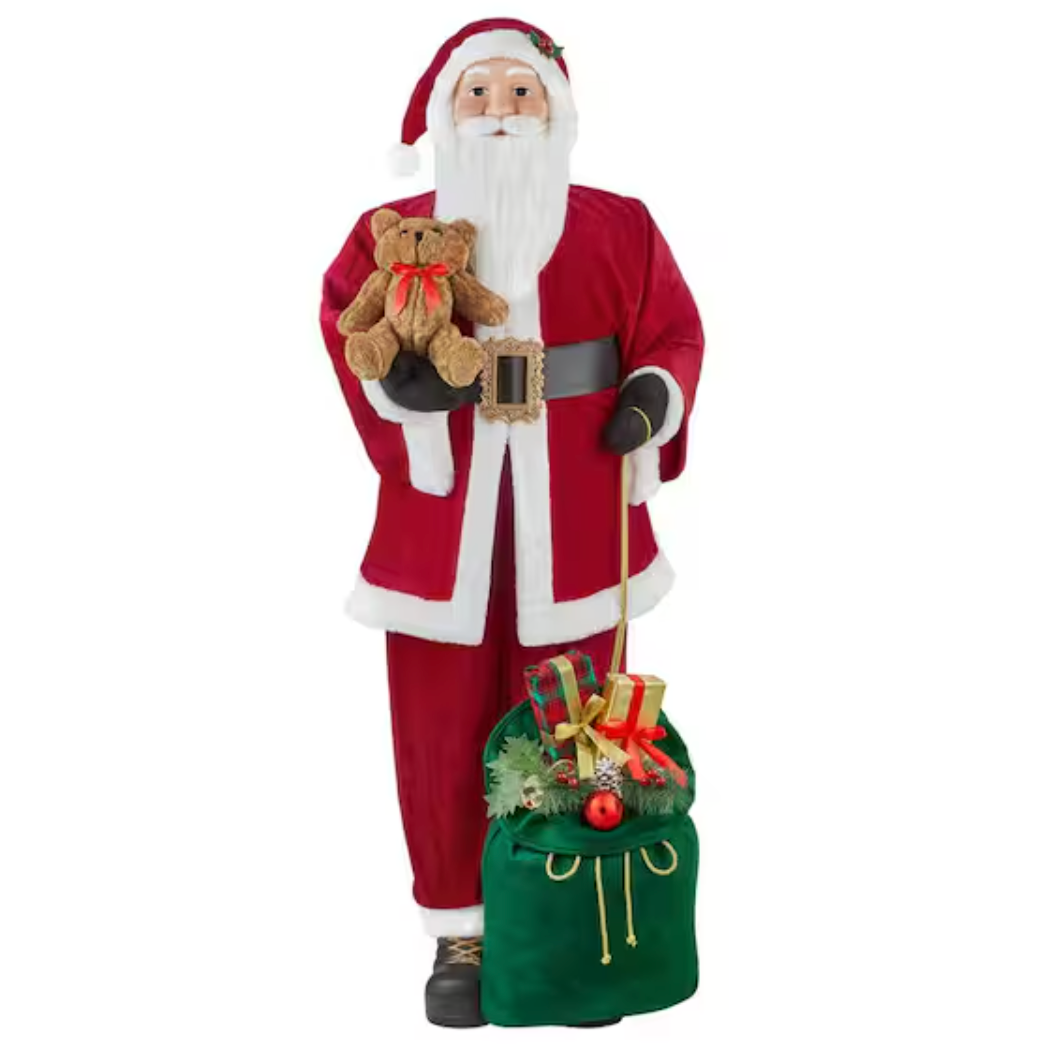 A 5-foot plush Santa Claus figure stands with a teddy bear in one hand and a green sack filled with presents in the other. Santa wears a red suit, black belt, and holds gold-detailed accessories.