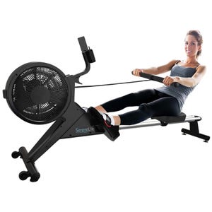 A SereneLife rowing machine with an air resistance system, featuring a sliding seat and foot straps. A woman is using the machine, demonstrating its ergonomic design for fitness training.