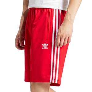 A person is wearing red Adidas shorts featuring white stripes and the Adidas Trefoil logo on the side.