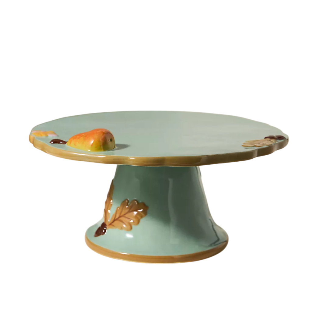 A decorative cake stand with a pale teal finish, featuring autumn leaf and small apple accents.