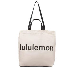 A beige tote bag with the \“lululemon\“ logo in black letters featuring two black straps.