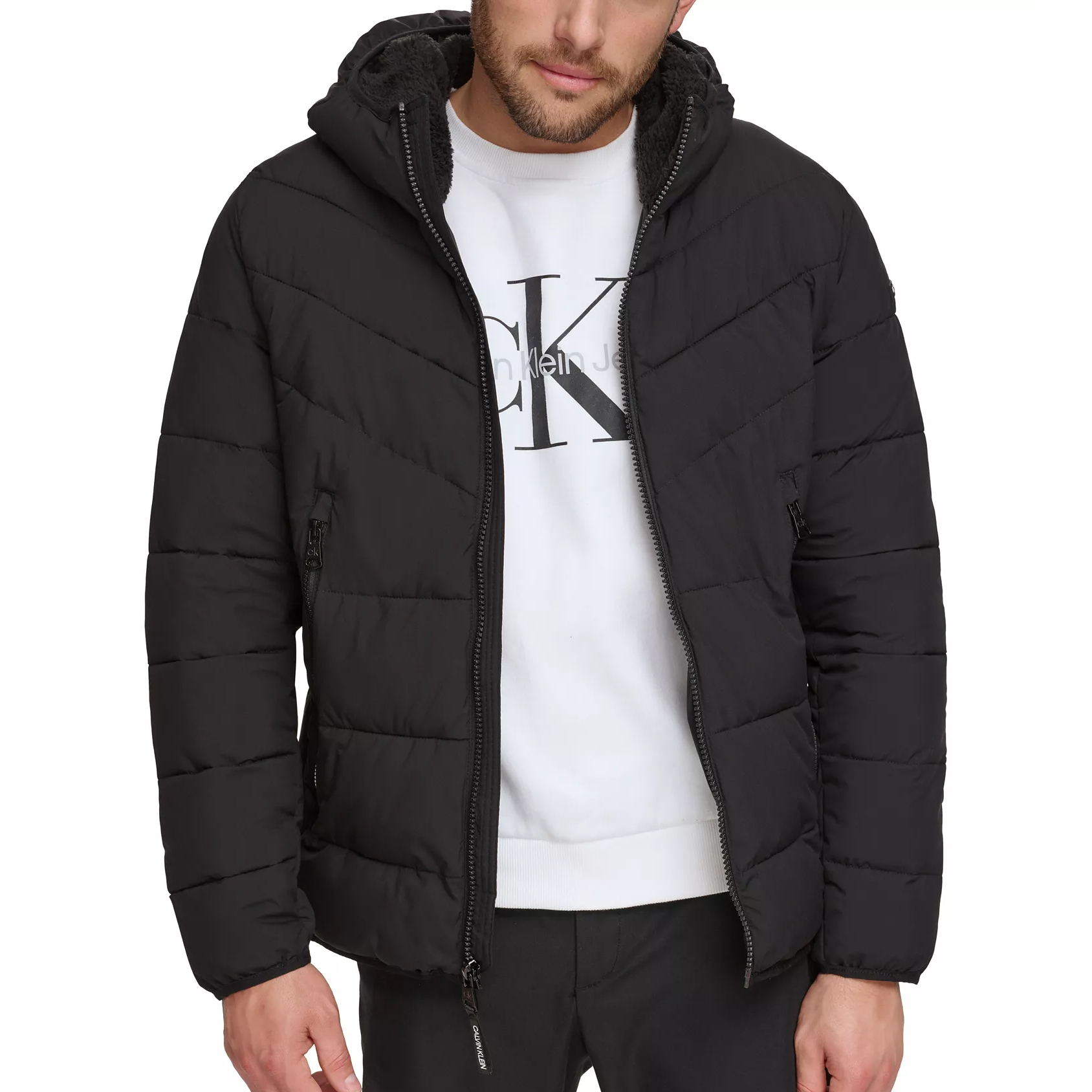 A man is wearing a black puffer jacket with a hood and a white sweatshirt featuring the Calvin Klein logo.