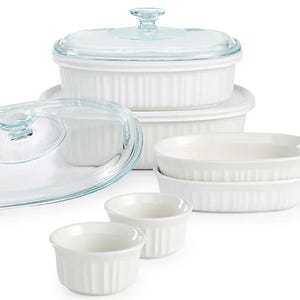 White Corningware bakeware set with clear glass lids includes round and oval casserole dishes, two smaller oval dishes, and three white ramekins. Each piece features a fluted design.
