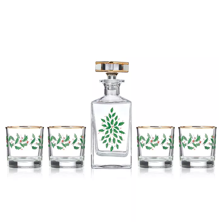 A set includes a whiskey decanter and four glasses, each adorned with green holly and red berry motifs and gold trim.