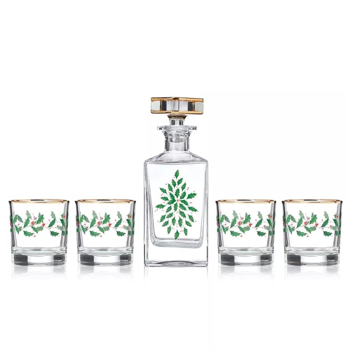 A set includes a whiskey decanter and four glasses, each adorned with green holly and red berry motifs and gold trim.