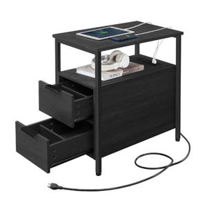A black side table with two open drawers and a top shelf holding a tablet, phone, and headphones. It features built-in charging ports, with a visible power cord extending from the back.