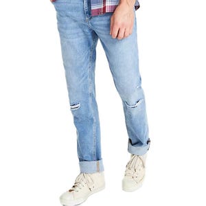 Light blue, distressed men's jeans with horizontal rips at the knees and a slightly faded wash. Worn with white sneakers and a plaid shirt tucked in at the front.