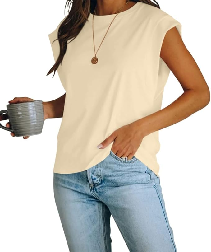 A person is wearing a sleeveless, light-colored top paired with light blue jeans, holding a mug, and accessorized with a simple pendant necklace.