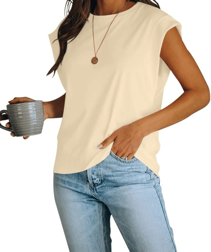 A person is wearing a sleeveless, light-colored top paired with light blue jeans, holding a mug, and accessorized with a simple pendant necklace.