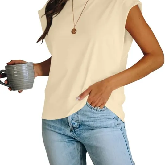 A person is wearing a sleeveless, light-colored top paired with light blue jeans, holding a mug, and accessorized with a simple pendant necklace.