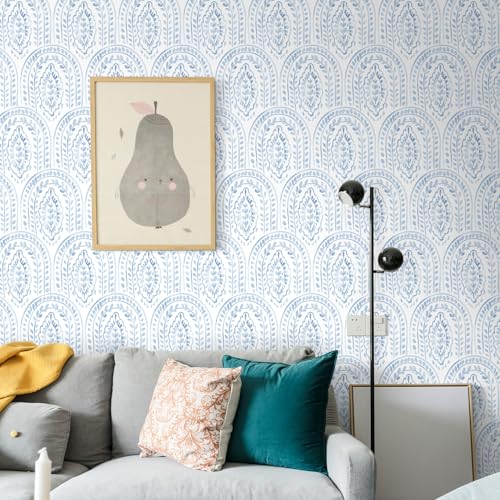 A modern living room features a gray sofa with colorful pillows, a yellow throw, a standing lamp, and a decorative wall with blue patterned wallpaper. A framed art piece depicting a pear is hung above the couch.