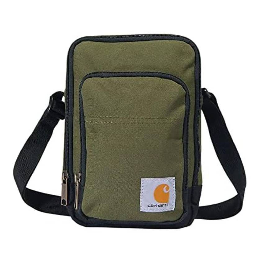A green Carhartt crossbody bag with a black strap and trim, featuring front and main zippered compartments and a logo patch at the bottom right.