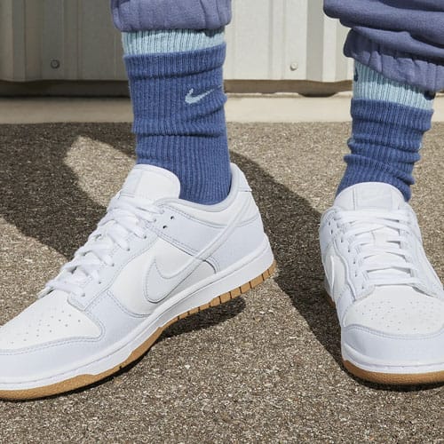 A pair of white Nike sneakers with a gum sole, matched with blue and white striped socks.